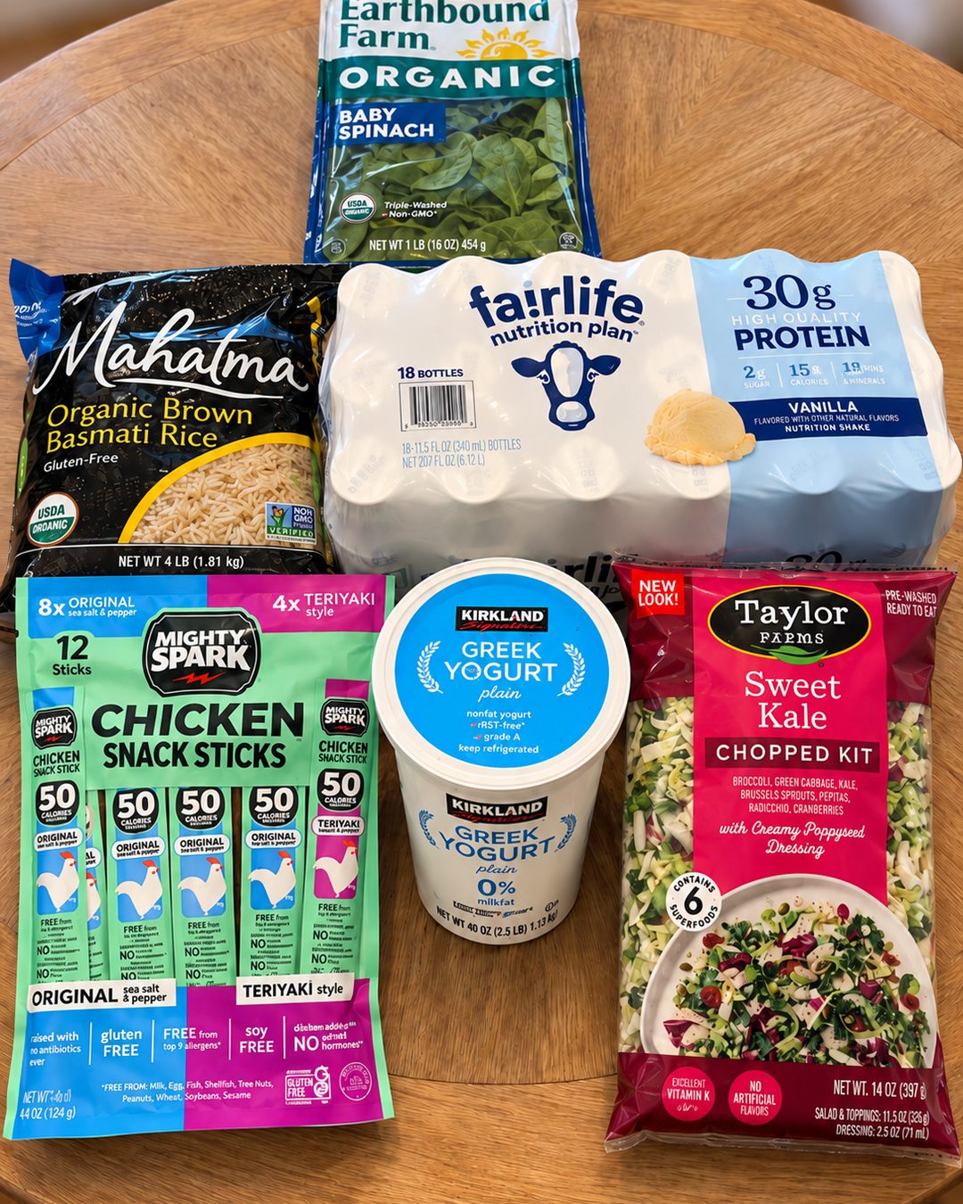 A group of Costco groceries including baby spinach, Fairlife protein shakes, chicken snack sticks, Greek yogurt and a Taylor Farms Sweet Kale chopped kit.